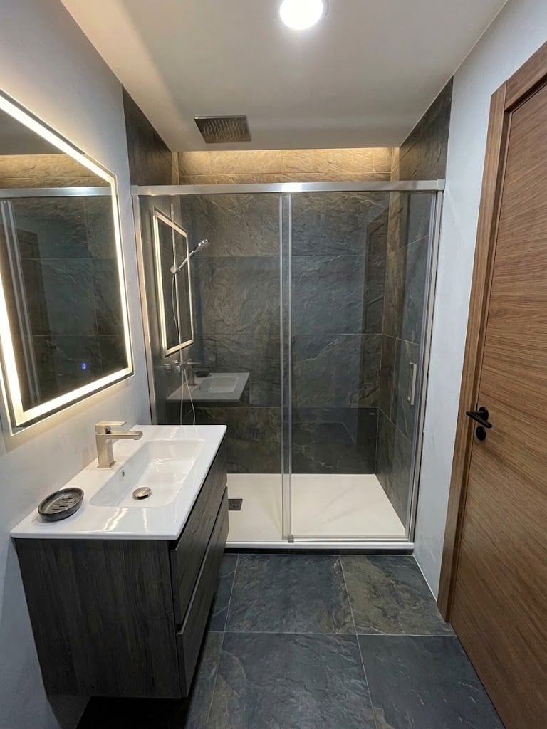 Baño reformado con ducha, gres oscuro y mueble de madera